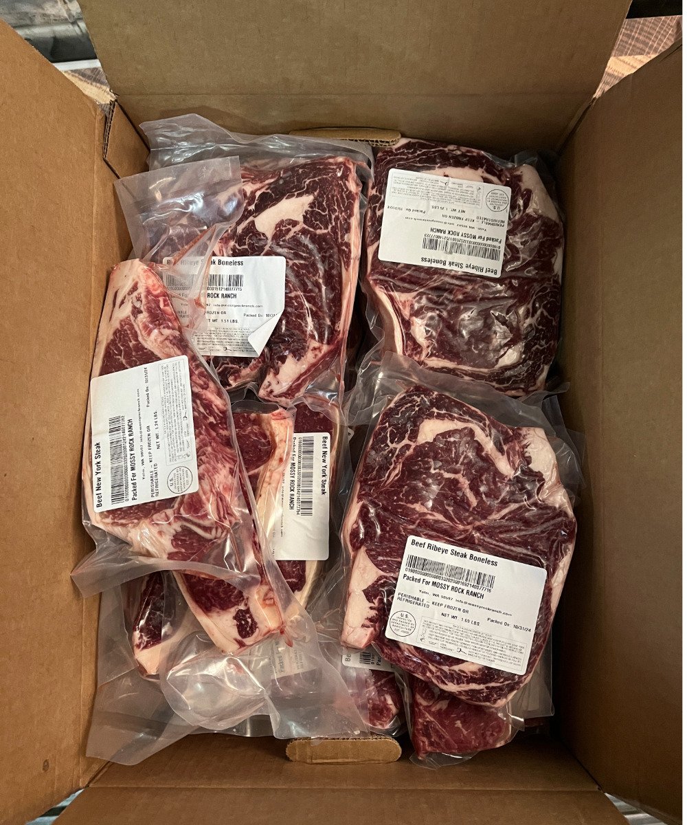 Box of vacuum-sealed boneless beef ribeye steaks, labeled and organized for freshness, showcasing high marbling and quality cuts, ideal for grilling or roasting.